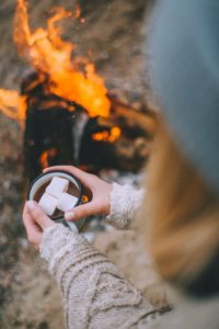 femme tenant une tasse de chocolat chaud auprès d'un feu