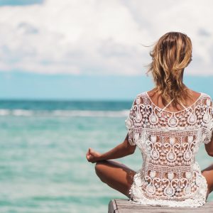 young woman meditation in a yoga pose at the beach